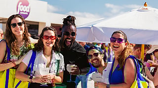 Group of friends smiling with drinks at SOBEWFF under a sunny beachside umbrella