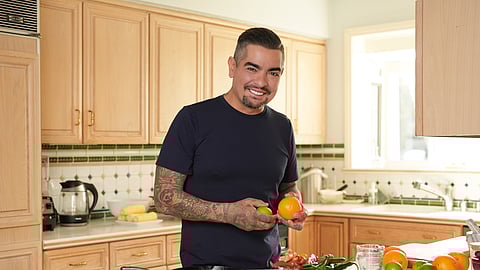 Chef Aarón Sánchez holding citrus in a bright home kitchen surrounded by fresh ingredients