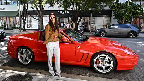 Julie Brangstrup stands beside a red Ferrari on a Miami street lined with luxury boutiques