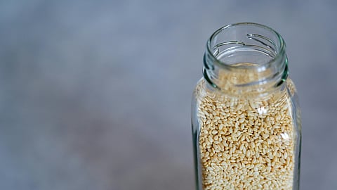 Close up of a glass jar packed with raw sesame seeds on a neutral background