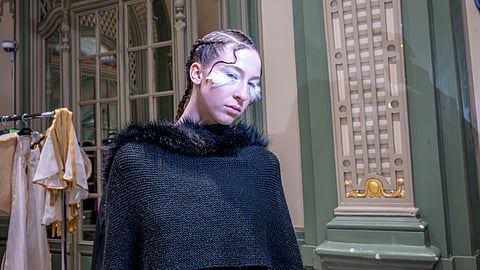 Model backstage in black knit couture with braided hair and white eye makeup