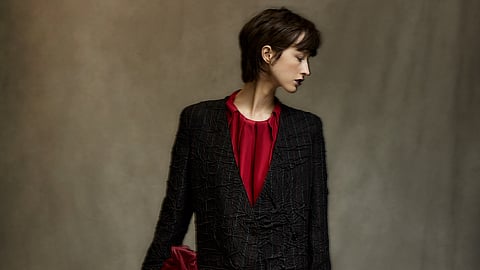Model in black crinkled suit with red blouse, asymmetrical hem, and brown boots
