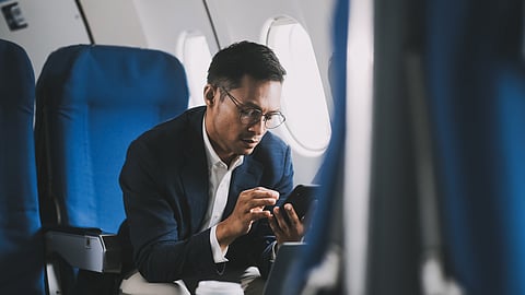 Man in airplane seat using smartphone while traveling with coffee and window light