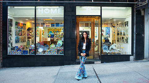 Elizabeth Sutton standing outside her Manhattan atelier storefront filled with colorful artwork