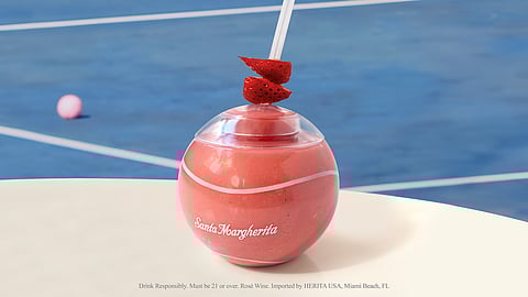 Pink frozen rosé cocktail in tennis ball cup on court backdrop with strawberries garnish