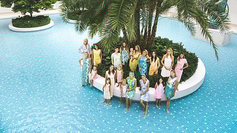 Women and children in Lilly Pulitzer dresses pose around a palm in a tiled fountain courtyard