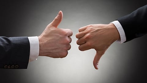 Two business professionals give opposing thumbs-up and thumbs-down gestures