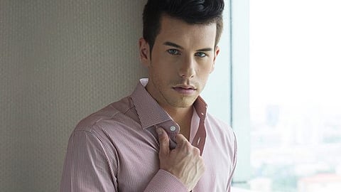 Man adjusting a tailored dress shirt near a window, showcasing fit and fabric detail