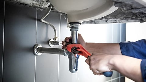 Person using wrench to fix plumbing pipes beneath a sink
