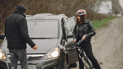 Cyclist wearing helmet stands next to car on roadside while speaking with driver