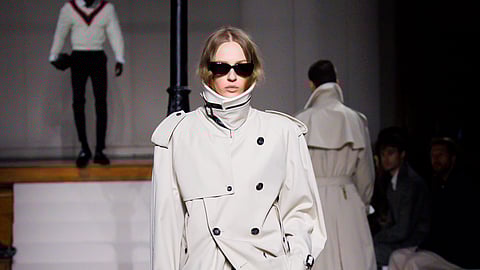 Model walks runway in structured white trench jacket with high collar and black skirt