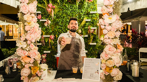 Bartender serving cocktail at floral booth with greenery backdrop