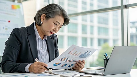 Professional analyzing charts and documents at a desk with laptop in office setting