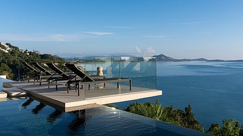 Infinity pool with lounge chairs overlooking ocean and tropical coastline