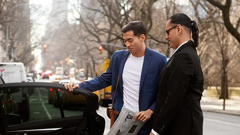 Two men standing beside a car on a city street, discussing a situation after opening the car door