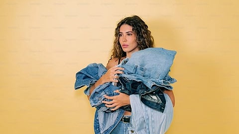 Woman holding a stack of folded denim clothing against a neutral background
