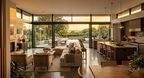 Luxury smart home living room and kitchen with floor-to-ceiling windows and sunset view.