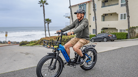 Man riding a folding electric bike along coastal road with ocean and homes in background