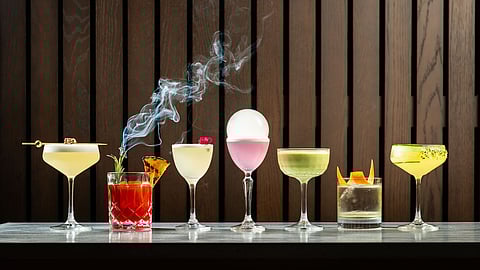 A lineup of crafted cocktails with smoke, citrus garnish, and glassware on a bar counter