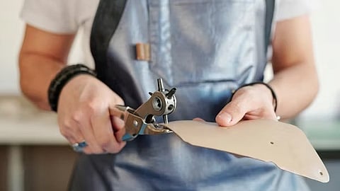 Hands cutting leather with tool in workshop showing craftsmanship process