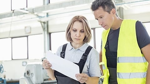 Two workers reviewing documents in industrial facility while discussing maintenance or operations