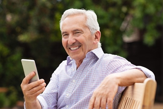 Smiling older man sitting outdoors holding smartphone and enjoying relaxed retirement lifestyle