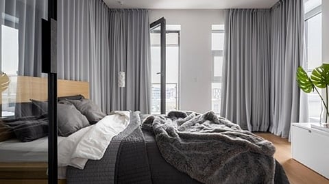 Minimalist bedroom with neutral tones, layered bedding, and soft natural light through curtains