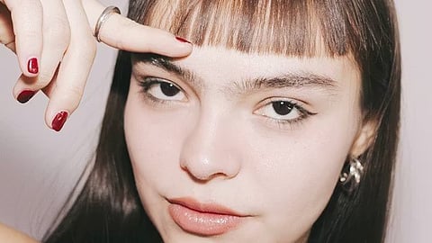 Woman with straight hair and short bangs pointing at fringe to highlight hairstyle choice