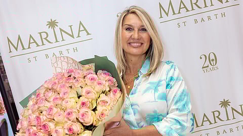 Marina Cocher holding bouquet of pink roses at Marina St Barth anniversary event backdrop