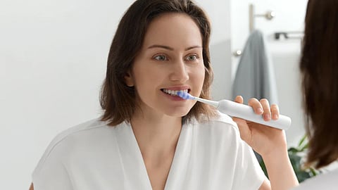 Woman brushing teeth with a smart electric toothbrush in a bright modern bathroom