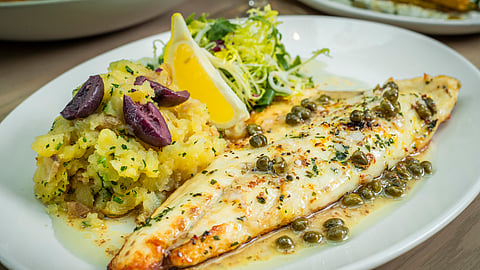 Branzino fillet with capers, lemon, and potatoes on a white plate
