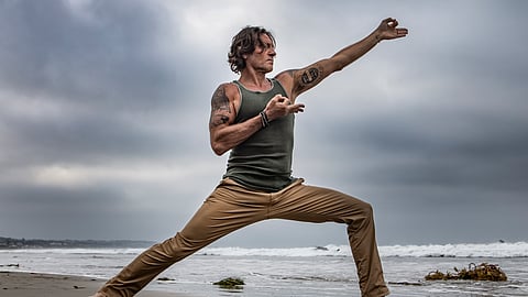 Eric Paskel performing a yoga pose on the beach under cloudy sky