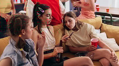 Group of young people sitting on a couch at a house party using a smartphone together