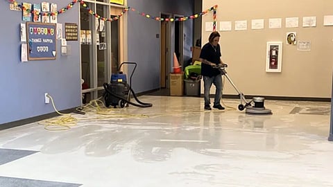 A commercial custodial worker deep cleaning a floor in a school