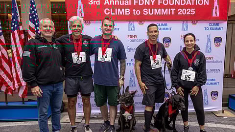Participants with medals and dogs pose at FDNY climb event backdrop in NYC
