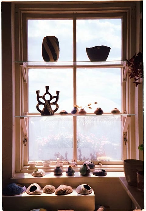 A collection of handcrafted ceramic pottery displayed on glass shelves and a windowsill