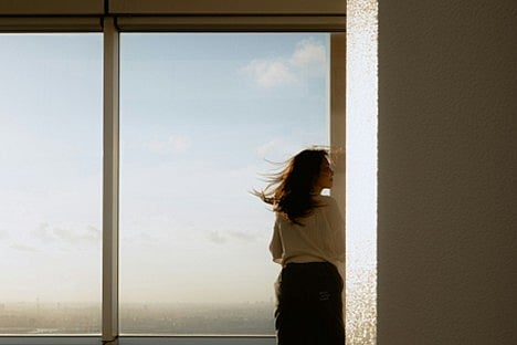 A person looking out a large window at a cityscape during sunset