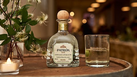 PATRÓN 100 tequila bottle displayed with a cocktail on a bar setting
