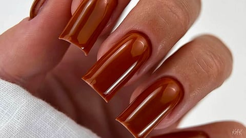 Medium-length, square-shaped nails painted in a glossy, dark amber jelly or burnt orange color