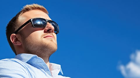 Man in sunglasses looking upward against clear blue sky in bright sunlight