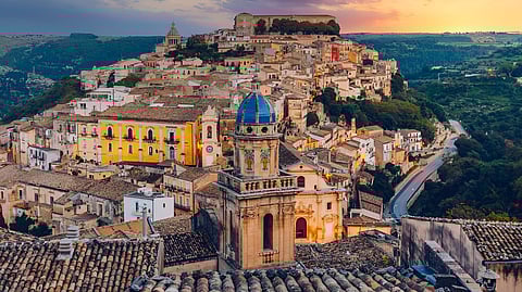 Hilltop Sicilian town with historic buildings and church dome at sunset