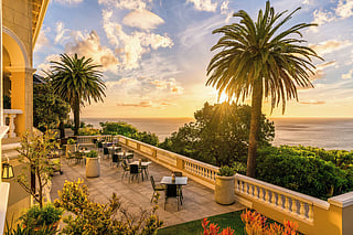 Ellerman House in Cape Town with palm trees, tables, and sunset views over the Atlantic Ocean.