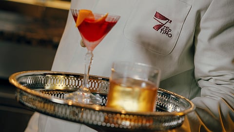 Server holding tray with red martini and whiskey cocktail in bar setting