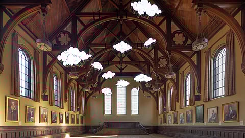 Illuminated cloud sculptures suspended from vaulted wooden ceiling in a historic gallery space