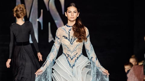 Model wearing a sheer embellished gown with flowing sleeves on runway