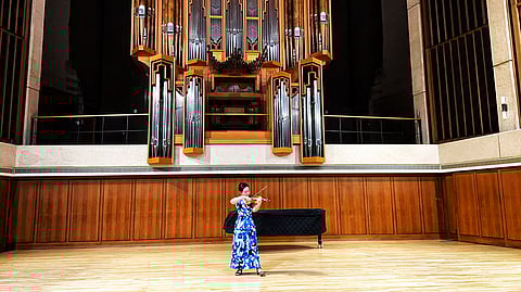 Violinist in blue dress performs solo on stage in concert hall with large pipe organ