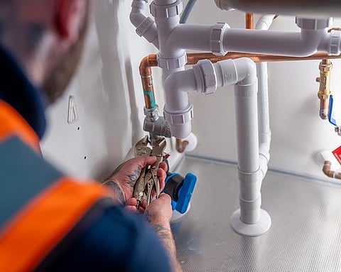 A plumber repairing or installing plumbing pipes under a sink