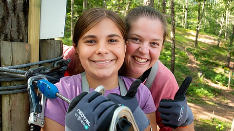 Mother and daughter with group wearing harnesses on treetop ropes course platform