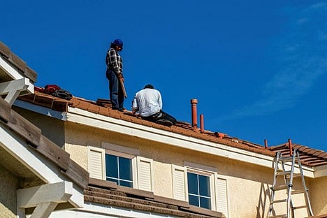 A moment of construction workers performing a tile roof repair on a residential house. 