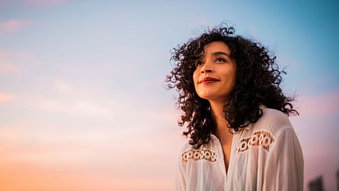 Woman with curly hair gazing upward at sunset sky with a peaceful expression